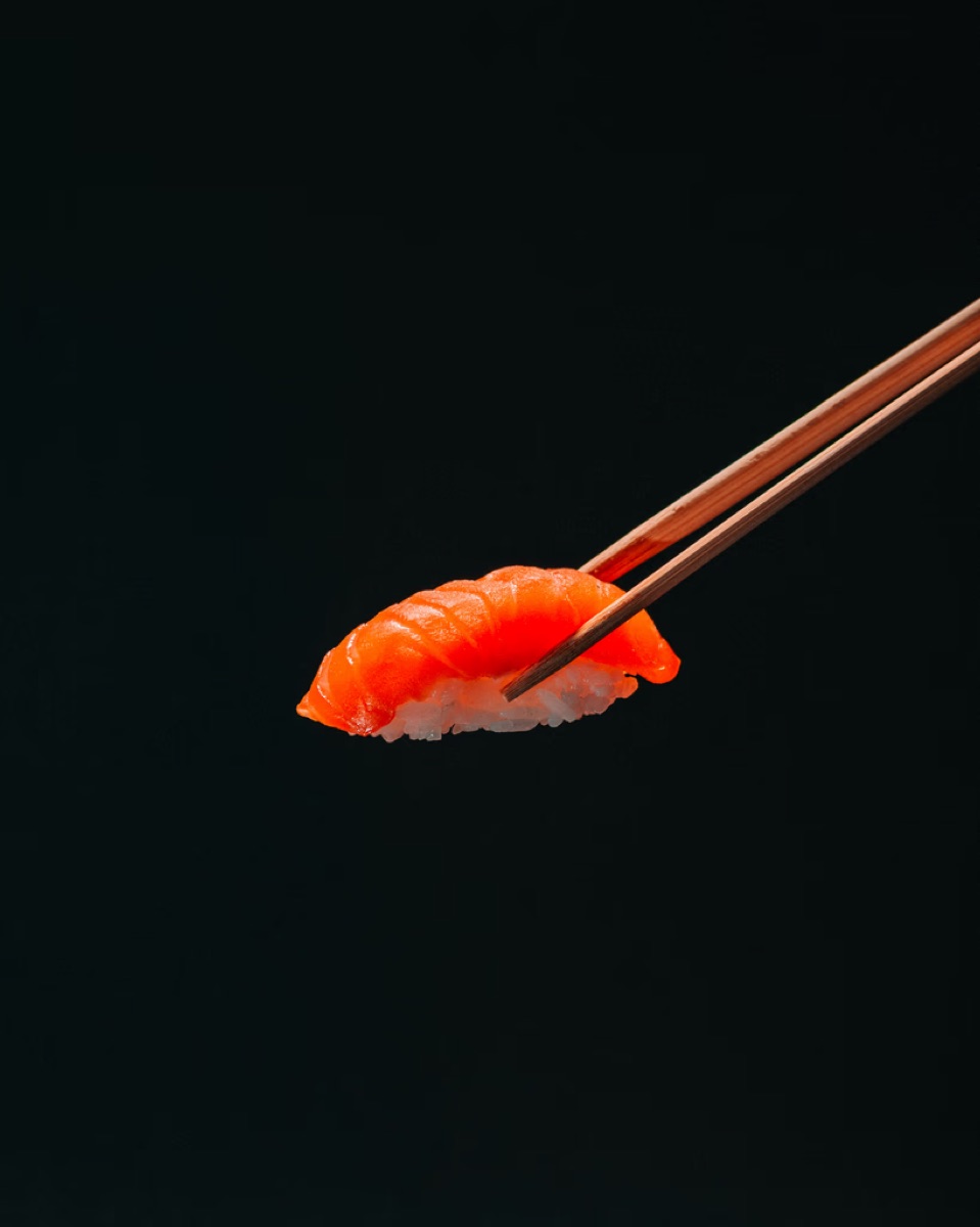 Lachs-Nigiri mit Essstäbchen vor dunklem Hintergrund